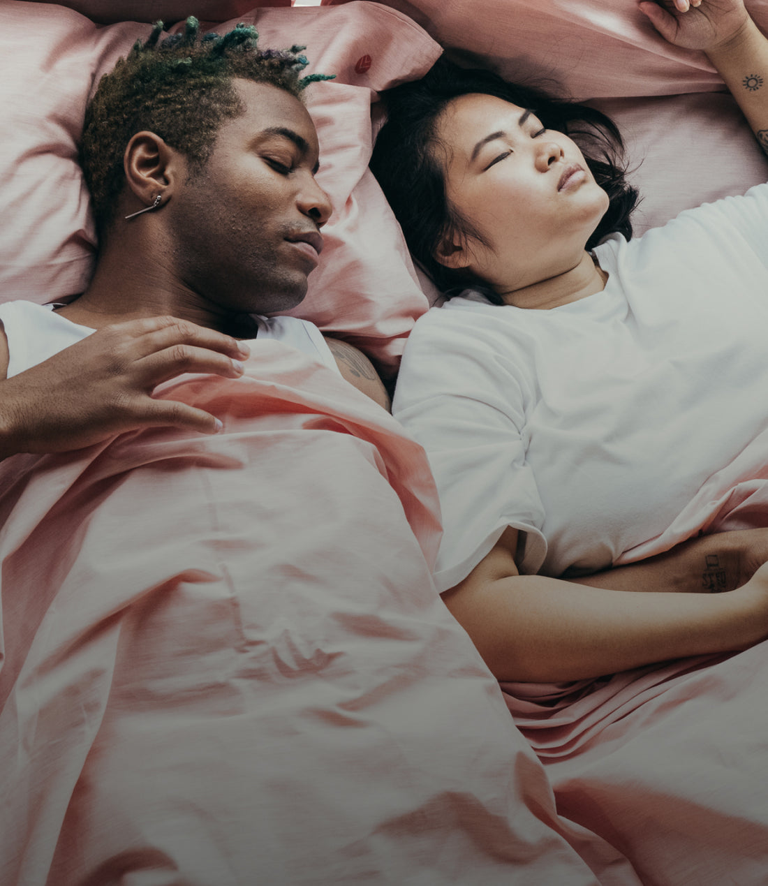 Two people lying in bed together with pink bedding.